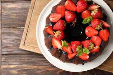 Photo of Delicious chocolate bundt cake with strawberries and mint on wooden table, top view