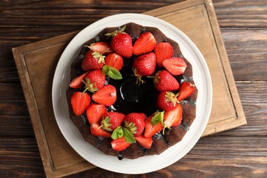 Photo of Delicious chocolate bundt cake with strawberries and mint on wooden table, top view