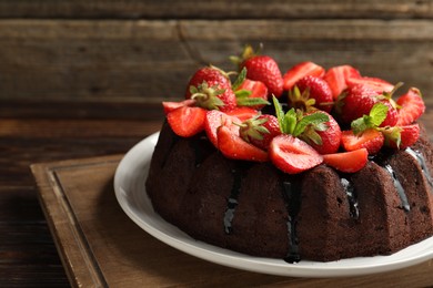 Photo of Delicious chocolate bundt cake with strawberries and mint on wooden table, closeup