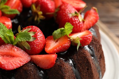 Photo of Delicious chocolate bundt cake with strawberries and mint on table, closeup