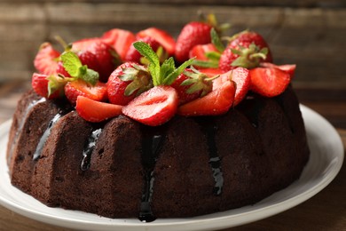 Photo of Delicious chocolate bundt cake with strawberries and mint on wooden table, closeup