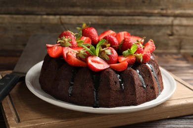 Photo of Delicious chocolate bundt cake with strawberries and mint on wooden table, closeup