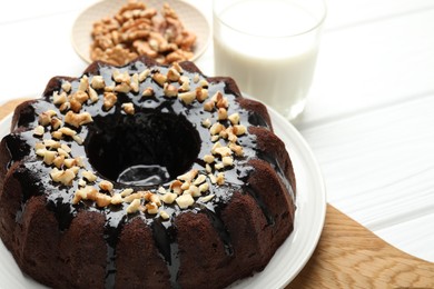 Photo of Delicious chocolate bundt cake with nuts and glass of milk on white wooden table, closeup