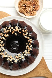 Photo of Delicious chocolate bundt cake with nuts and glass of milk on white wooden table, flat lay