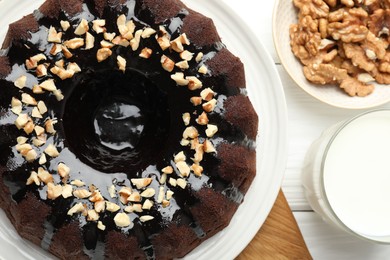 Photo of Delicious chocolate bundt cake with nuts and glass of milk on white wooden table, flat lay