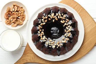 Photo of Delicious chocolate bundt cake with nuts and glass of milk on white wooden table, flat lay