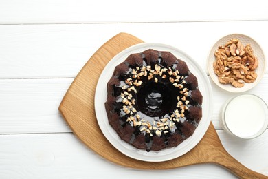 Photo of Delicious chocolate bundt cake with nuts and glass of milk on white wooden table, flat lay