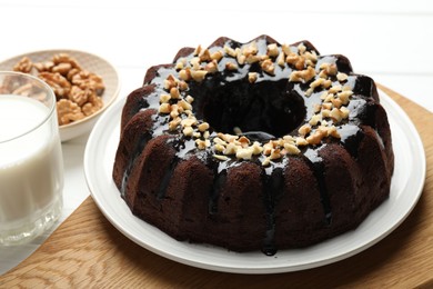 Photo of Delicious chocolate bundt cake with nuts and glass of milk on white wooden table, closeup
