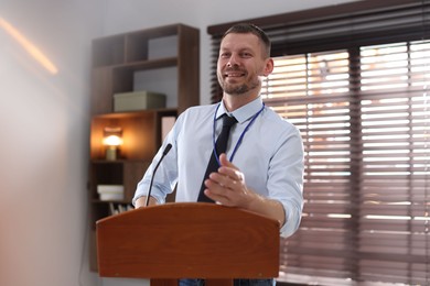 Photo of Man giving public speech with microphone at lectern indoors