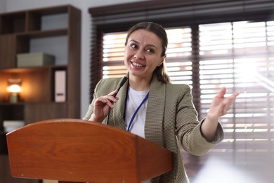 Photo of Woman giving public speech with microphone at lectern indoors
