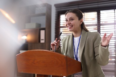 Photo of Woman giving public speech with microphone at lectern indoors