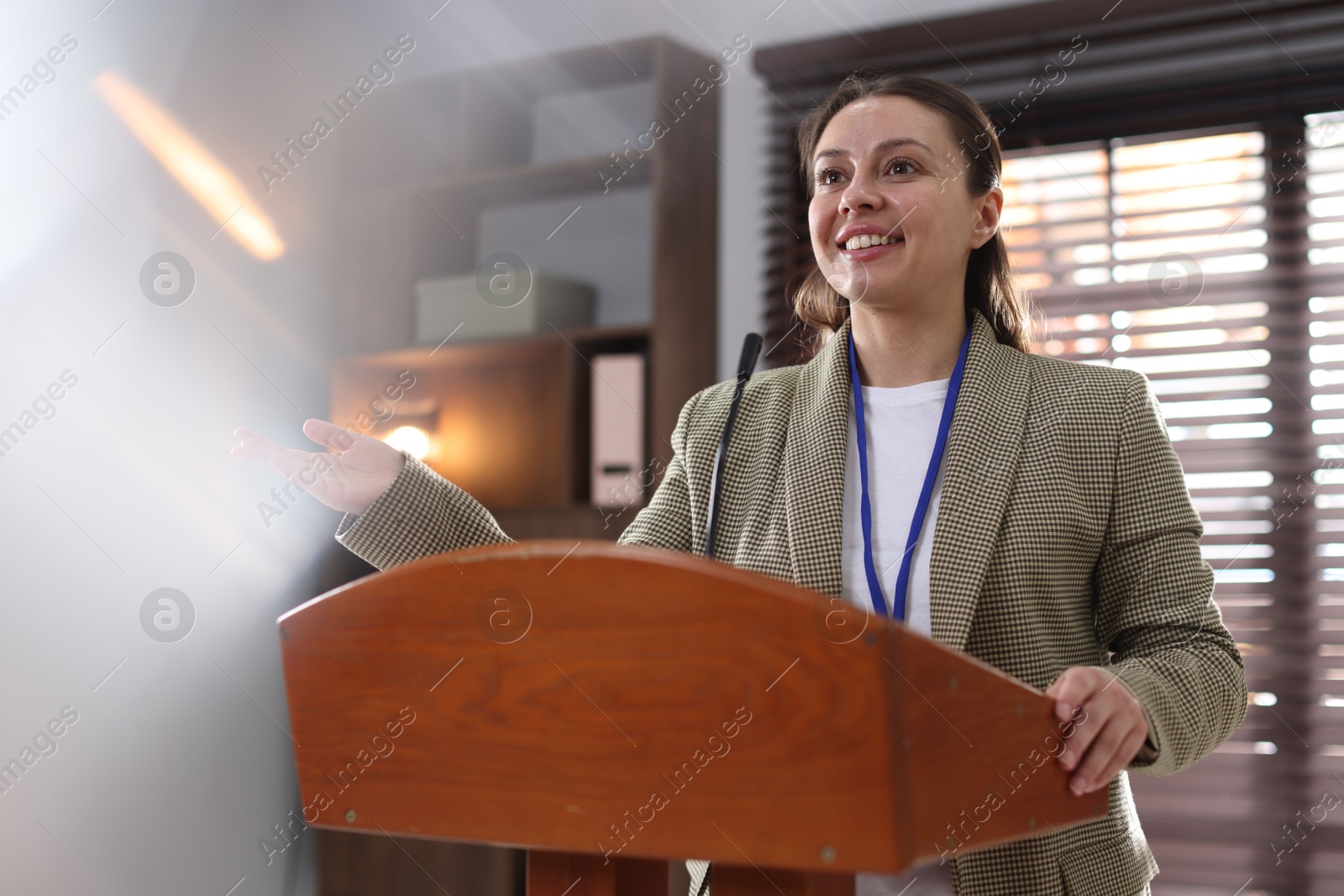 Woman giving public speech with microphone at lectern indoors Photo of Woman giving public speech with microphone at lectern indoors