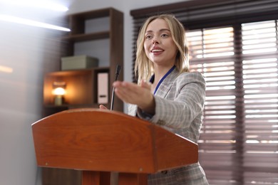 Photo of Woman giving public speech with microphone at lectern indoors