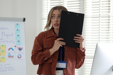 Photo of Fear of public speaking. Nervous woman with clipboard indoors