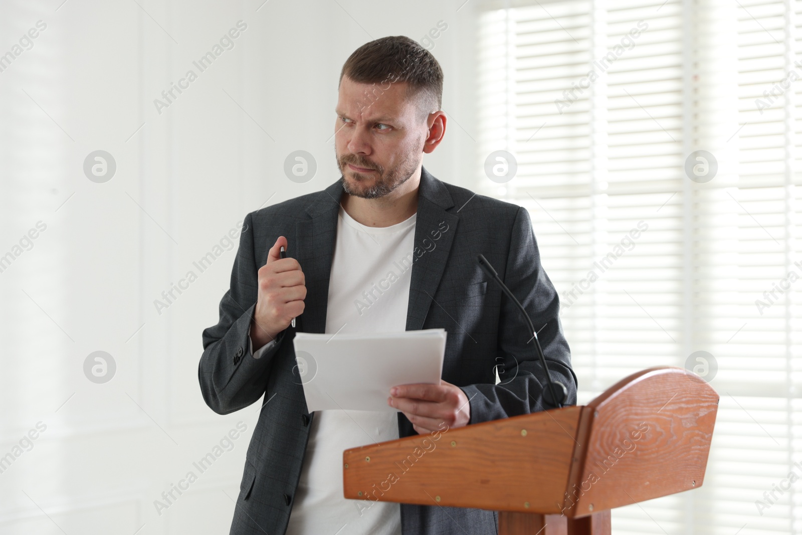 Fear of public speaking. Nervous man with microphone at lectern indoors Photo of Fear of public speaking. Nervous man with microphone at lectern indoors