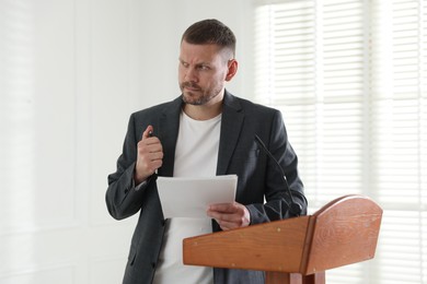 Photo of Fear of public speaking. Nervous man with microphone at lectern indoors