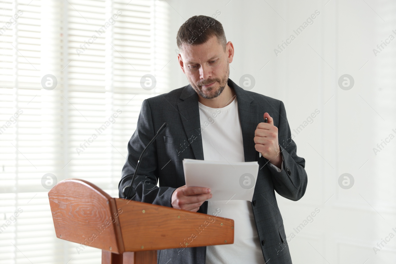 Fear of public speaking. Nervous man with microphone at lectern indoors Photo of Fear of public speaking. Nervous man with microphone at lectern indoors