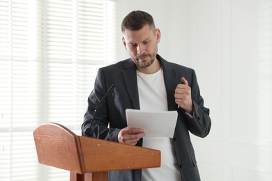 Photo of Fear of public speaking. Nervous man with microphone at lectern indoors