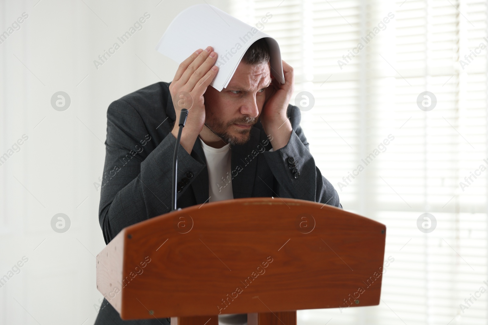 Fear of public speaking. Nervous man with microphone at lectern indoors Photo of Fear of public speaking. Nervous man with microphone at lectern indoors