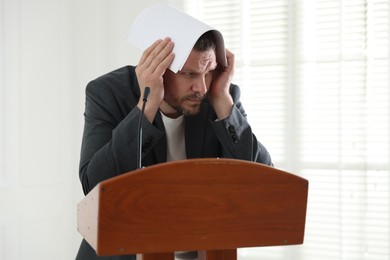 Photo of Fear of public speaking. Nervous man with microphone at lectern indoors