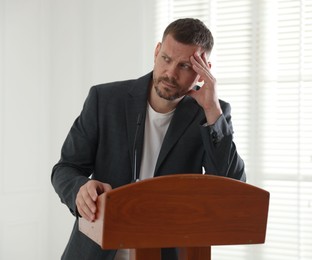 Photo of Fear of public speaking. Nervous man with microphone at lectern indoors