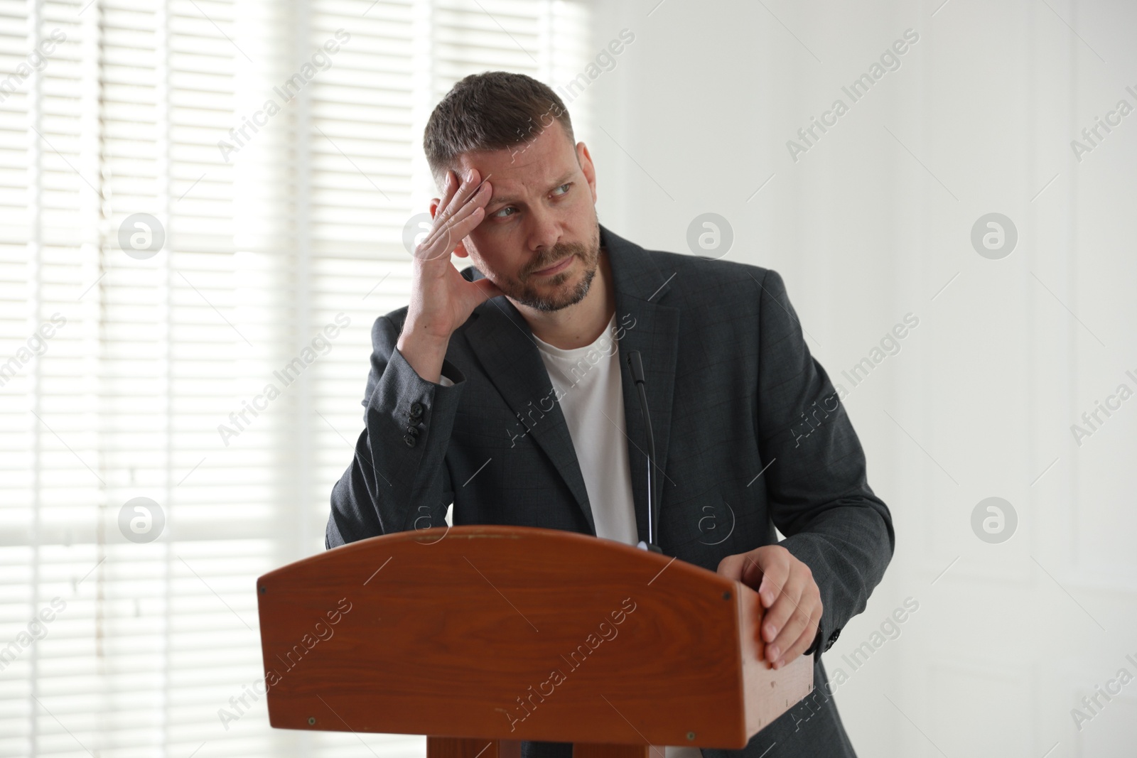 Fear of public speaking. Nervous man with microphone at lectern indoors Photo of Fear of public speaking. Nervous man with microphone at lectern indoors