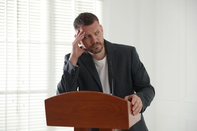 Photo of Fear of public speaking. Nervous man with microphone at lectern indoors