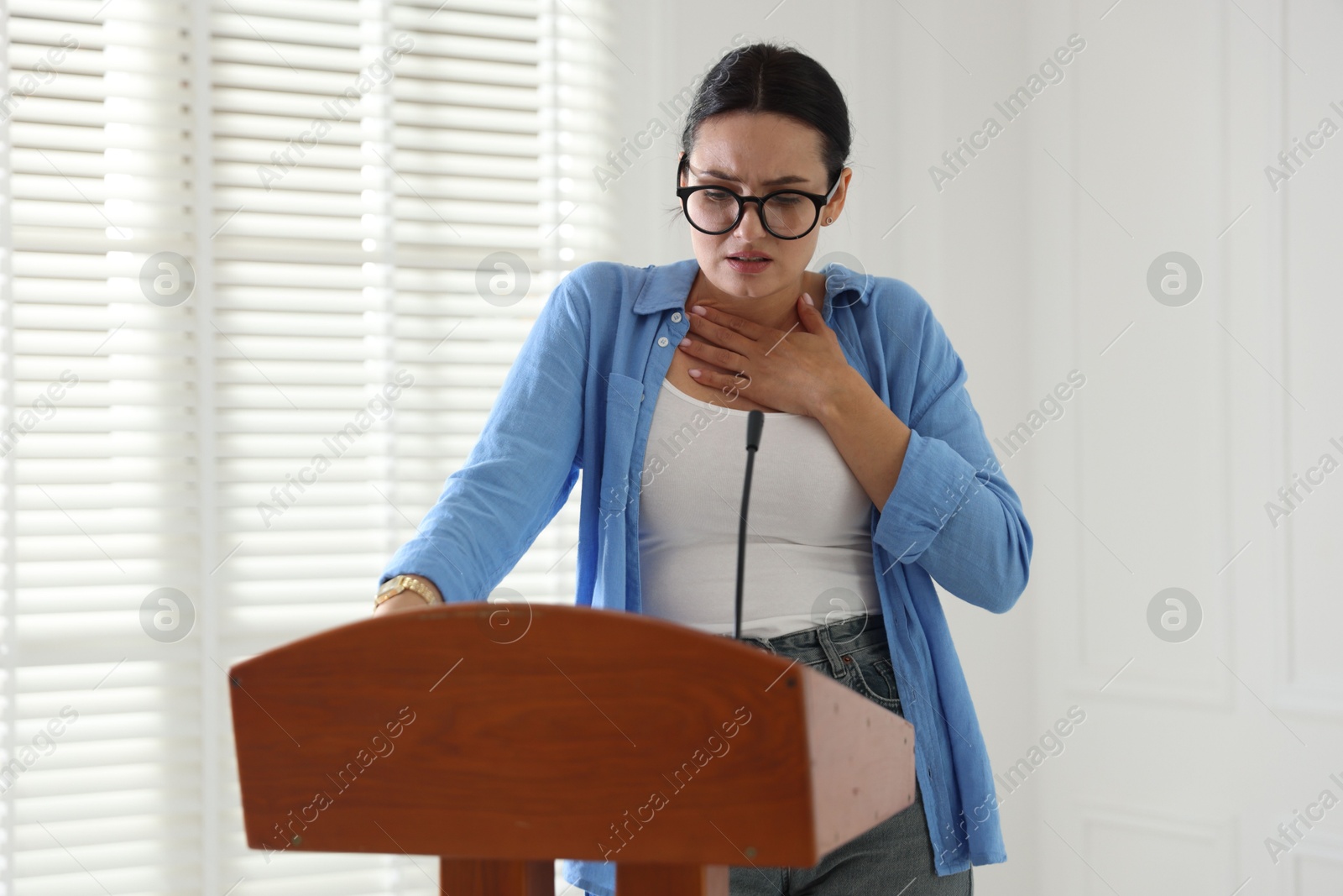 Fear of public speaking. Nervous woman with microphone at lectern indoors Photo of Fear of public speaking. Nervous woman with microphone at lectern indoors