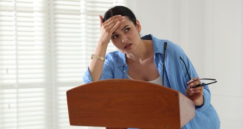 Photo of Fear of public speaking. Nervous woman with microphone at lectern indoors