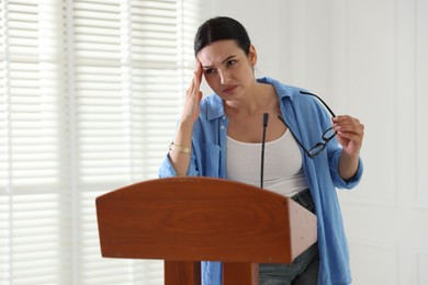Photo of Fear of public speaking. Nervous woman with microphone at lectern indoors