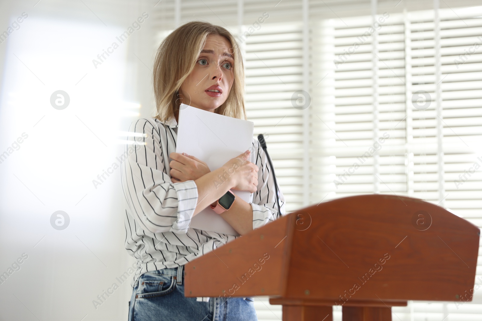 Fear of public speaking. Nervous woman with microphone at lectern indoors Photo of Fear of public speaking. Nervous woman with microphone at lectern indoors