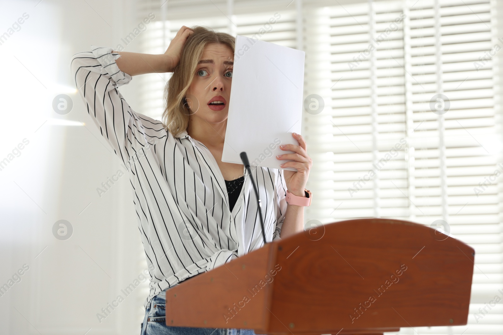 Fear of public speaking. Nervous woman with microphone at lectern indoors Photo of Fear of public speaking. Nervous woman with microphone at lectern indoors