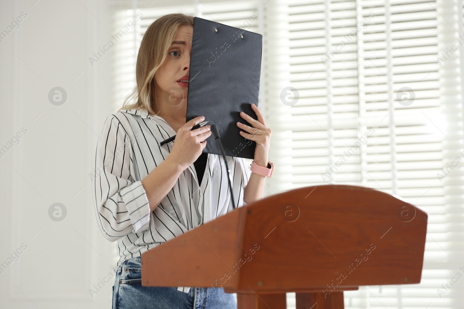 Fear of public speaking. Nervous woman with microphone at lectern indoors Photo of Fear of public speaking. Nervous woman with microphone at lectern indoors