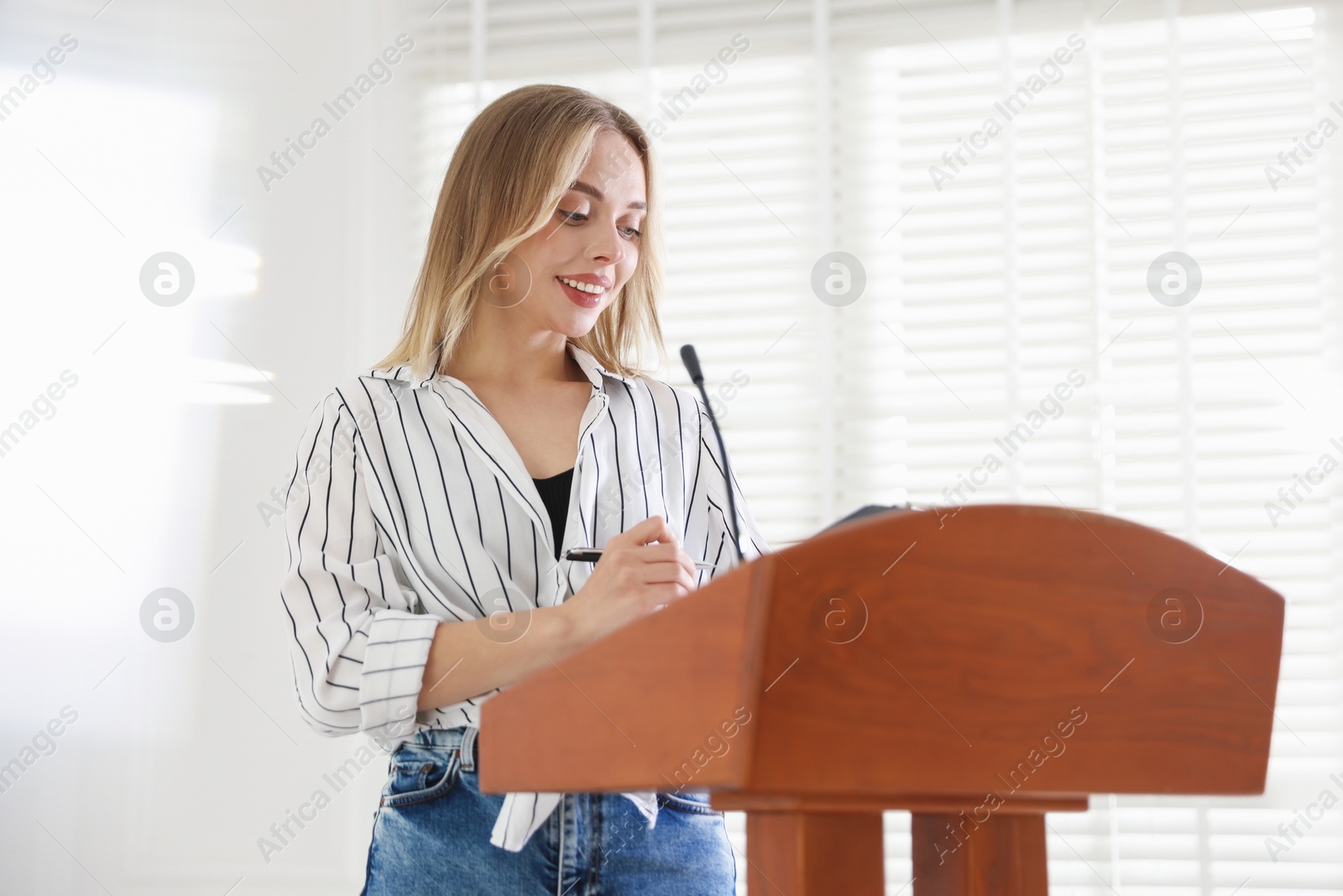 Woman giving public speech with microphone at lectern indoors Photo of Woman giving public speech with microphone at lectern indoors