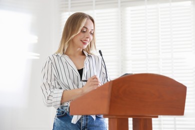 Photo of Woman giving public speech with microphone at lectern indoors