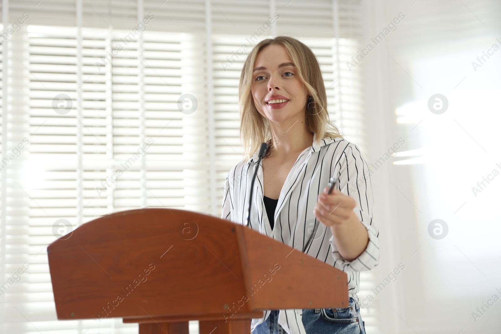 Woman giving public speech with microphone at lectern indoors Photo of Woman giving public speech with microphone at lectern indoors