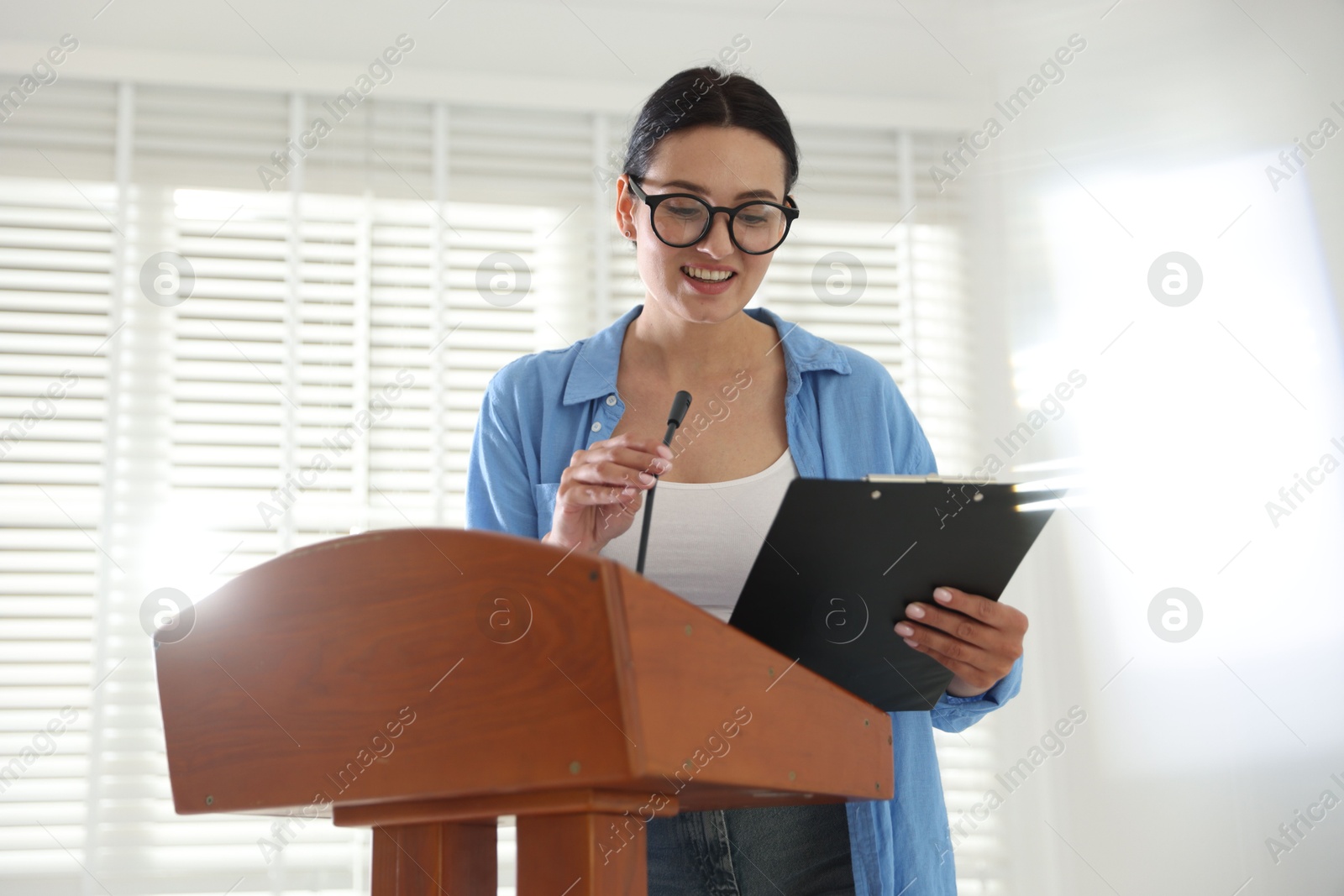 Woman giving public speech with microphone at lectern indoors Photo of Woman giving public speech with microphone at lectern indoors