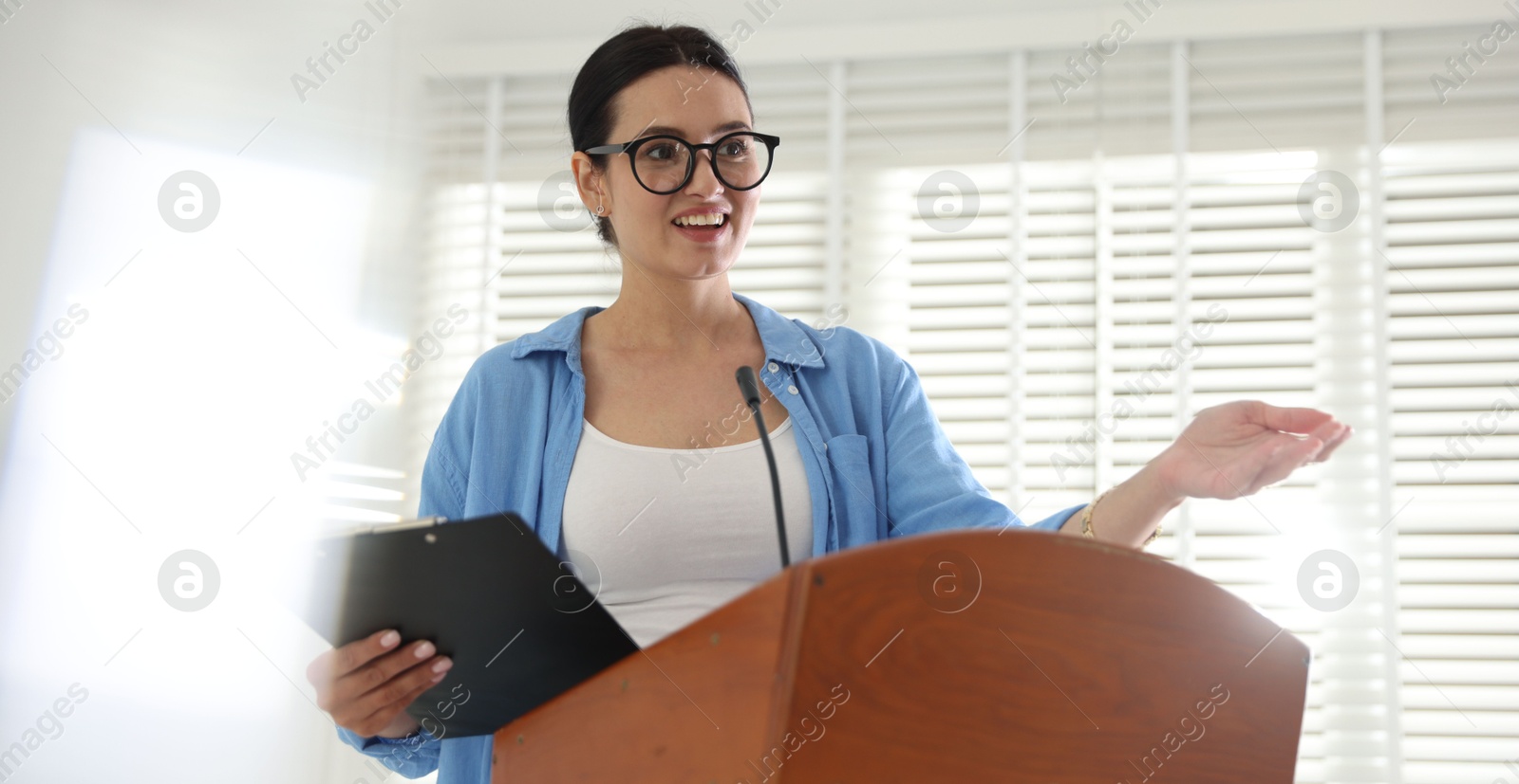 Woman giving public speech with microphone at lectern indoors Photo of Woman giving public speech with microphone at lectern indoors