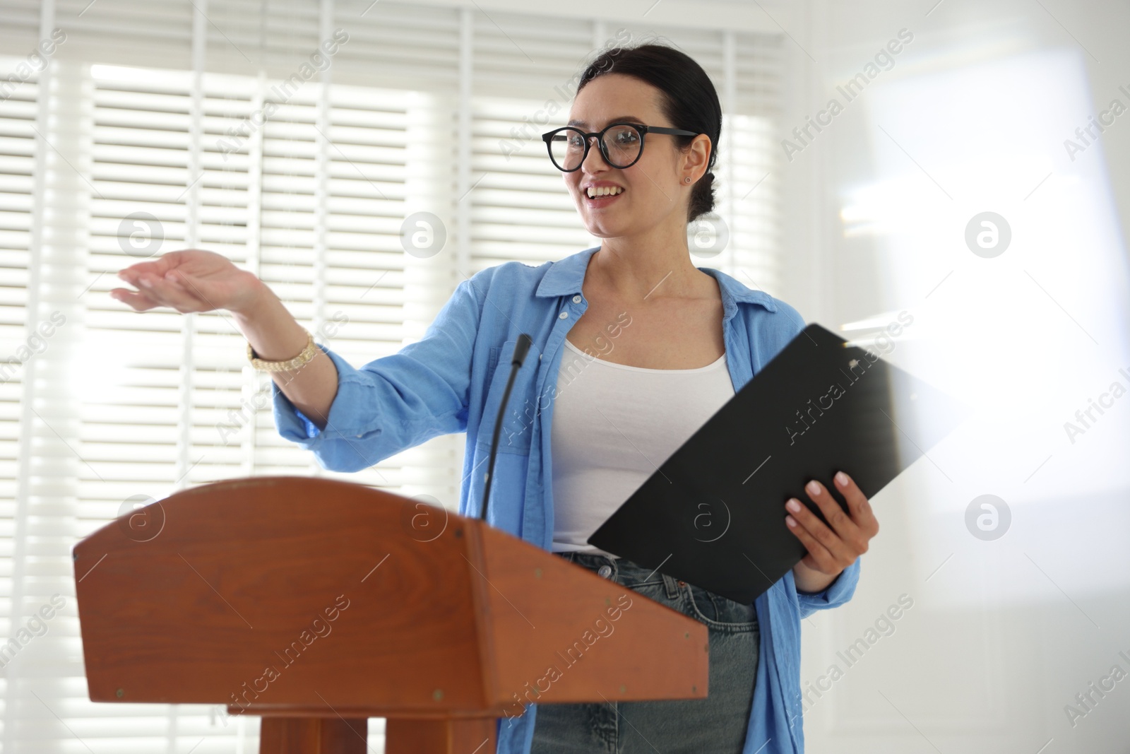 Woman giving public speech with microphone at lectern indoors Photo of Woman giving public speech with microphone at lectern indoors