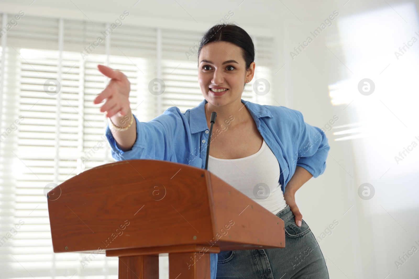 Woman giving public speech with microphone at lectern indoors Photo of Woman giving public speech with microphone at lectern indoors