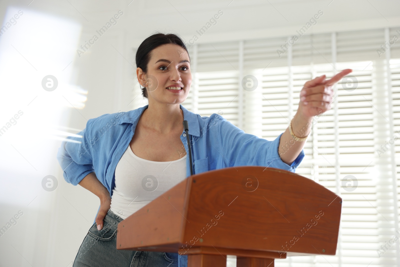 Woman giving public speech with microphone at lectern indoors Photo of Woman giving public speech with microphone at lectern indoors