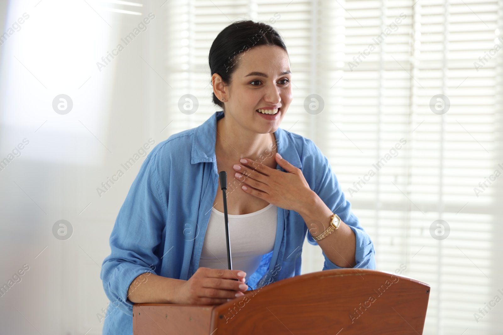 Woman giving public speech with microphone at lectern indoors Photo of Woman giving public speech with microphone at lectern indoors