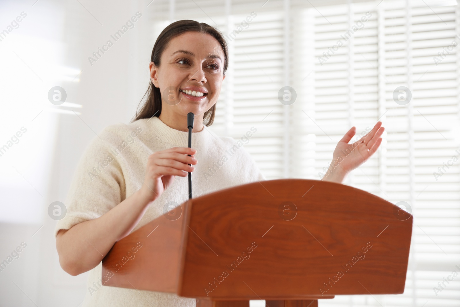 Woman giving public speech with microphone at lectern indoors Photo of Woman giving public speech with microphone at lectern indoors