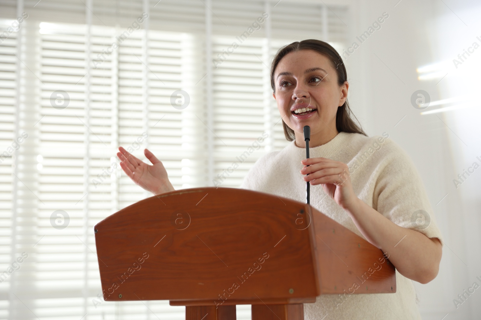 Woman giving public speech with microphone at lectern indoors Photo of Woman giving public speech with microphone at lectern indoors