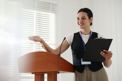 Photo of Woman giving public speech with microphone at lectern indoors