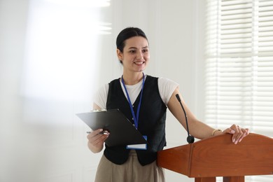 Photo of Woman giving public speech with microphone at lectern indoors