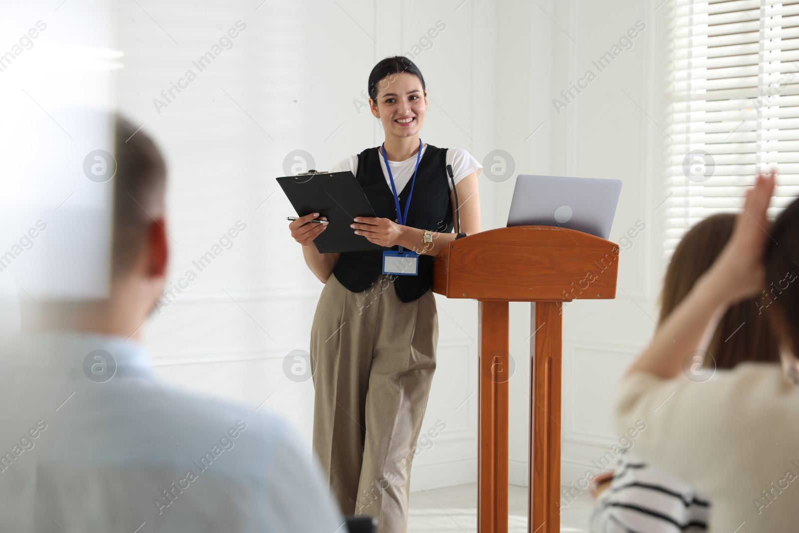 Woman giving public speech at lectern in front of audience indoors Photo of Woman giving public speech at lectern in front of audience indoors