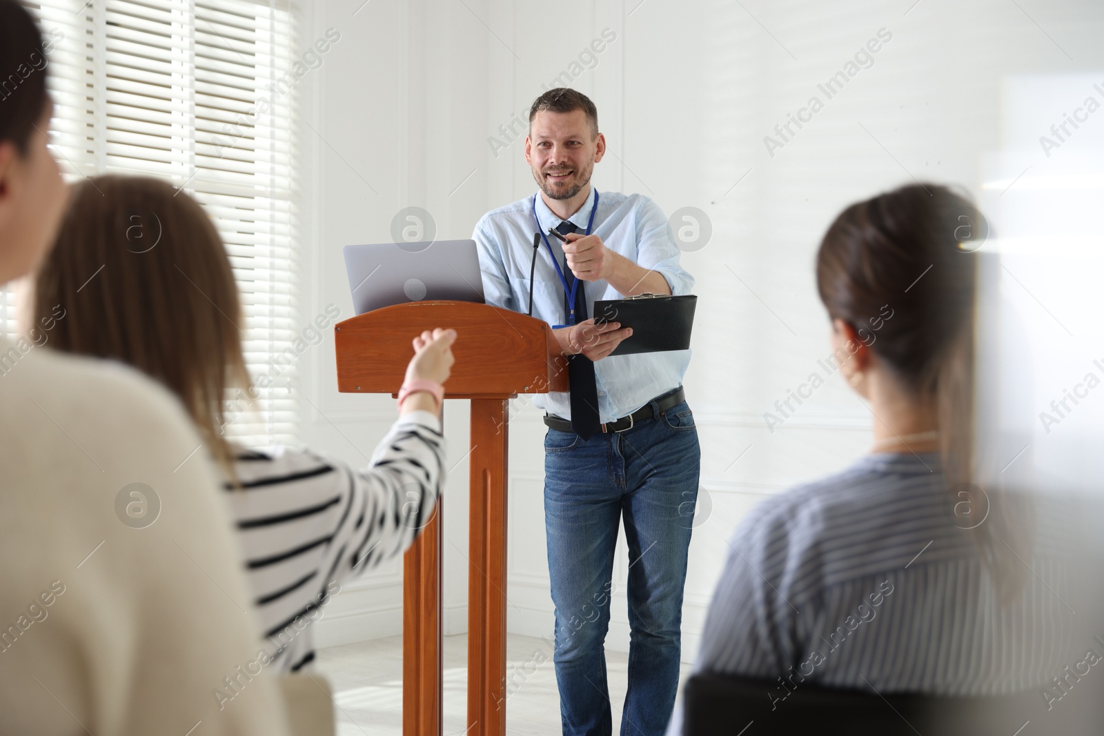 Photo of Man giving public speech at lectern in front of audience indoors