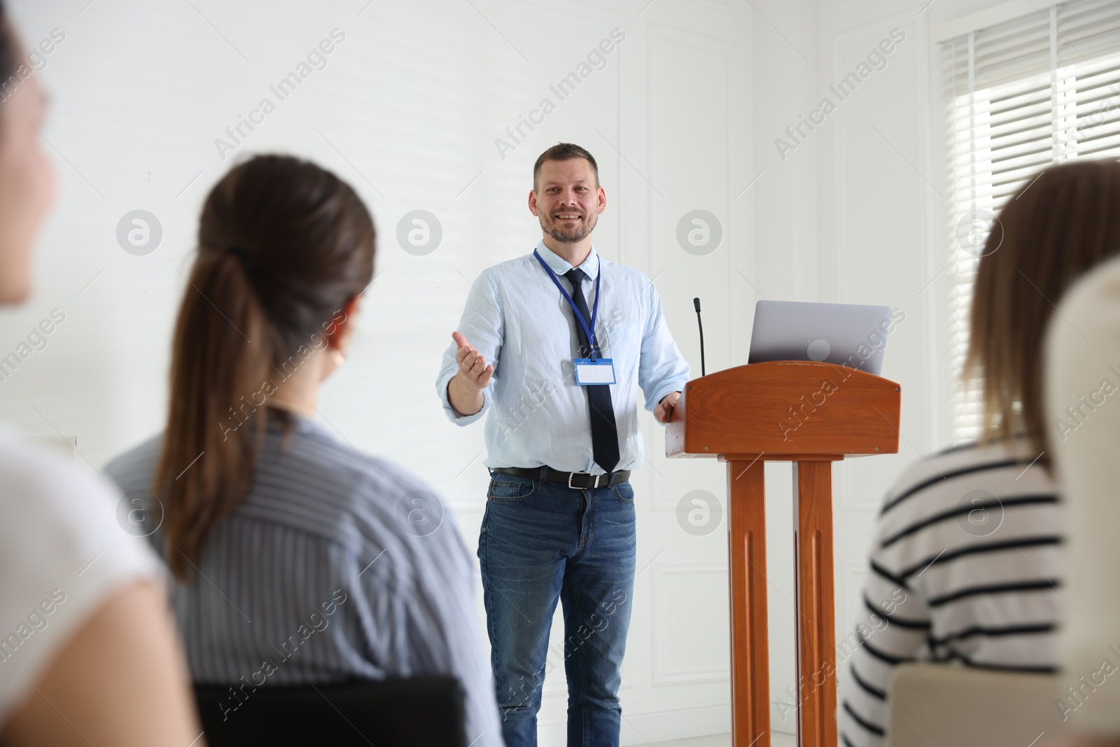 Photo of Man giving public speech at lectern in front of audience indoors