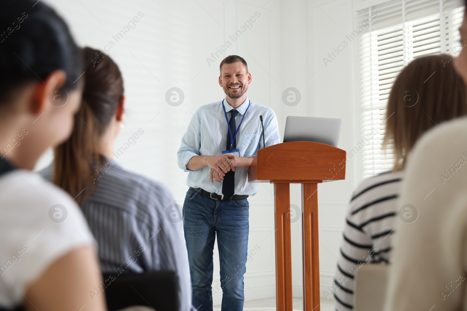 Photo of Man giving public speech at lectern in front of audience indoors